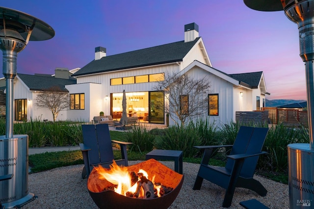 back of house featuring board and batten siding, an outdoor fire pit, a patio area, and a chimney