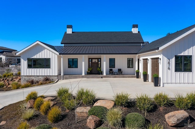 rear view of property with board and batten siding, a standing seam roof, driveway, and metal roof