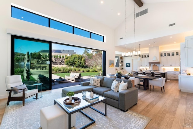 living area featuring light wood finished floors, beamed ceiling, visible vents, and a notable chandelier