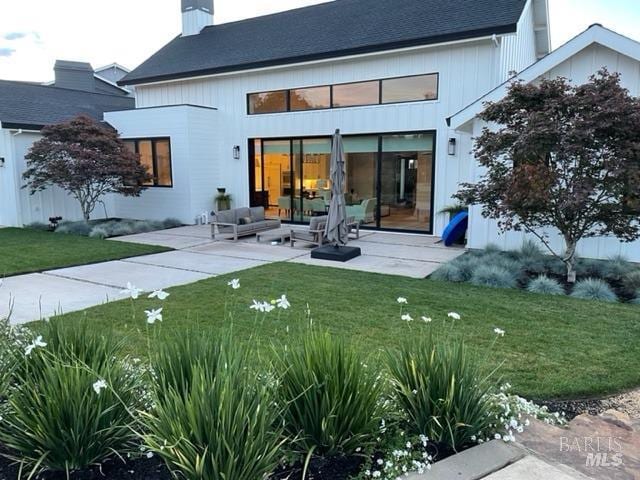 rear view of property featuring a patio, a lawn, and a chimney