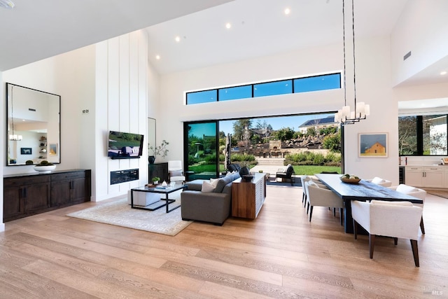 living area featuring recessed lighting, a towering ceiling, light wood-style flooring, and a notable chandelier