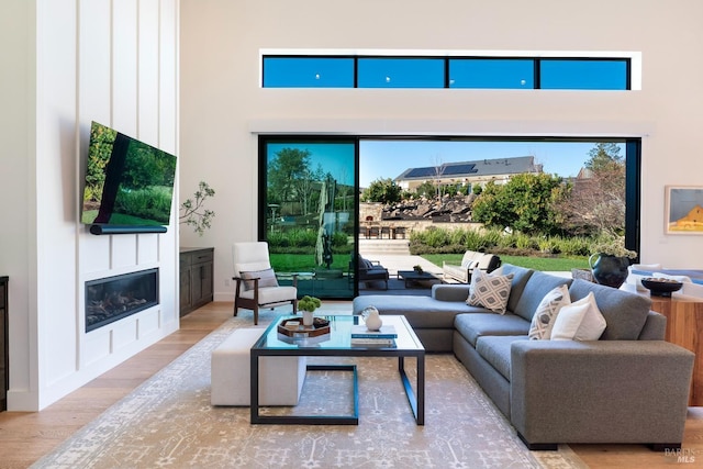 living room with plenty of natural light, a high ceiling, wood finished floors, and a glass covered fireplace