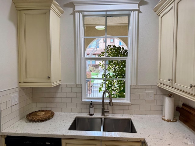 kitchen featuring decorative backsplash, cream cabinets, a sink, and dishwasher