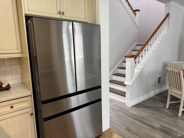 kitchen with visible vents, light stone counters, wood finished floors, freestanding refrigerator, and backsplash