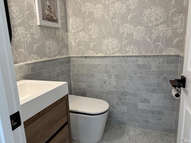 half bathroom featuring toilet, wainscoting, tile walls, and vanity