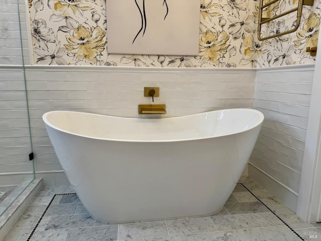 bathroom featuring wallpapered walls, a freestanding tub, and a wainscoted wall