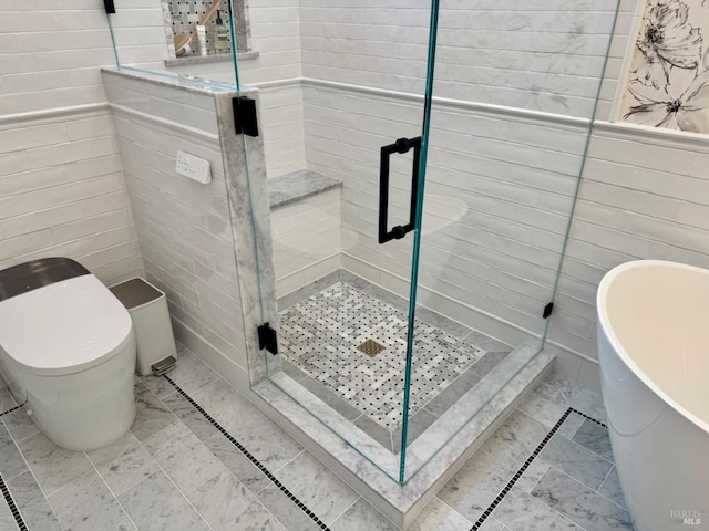 bathroom with a stall shower, a freestanding bath, tile walls, and toilet