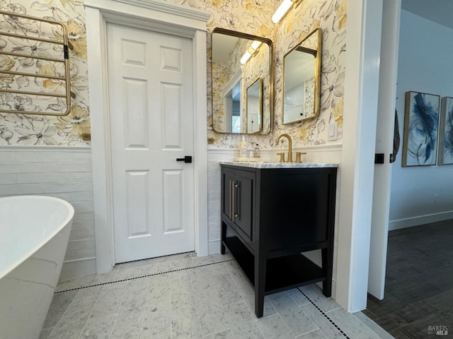 full bathroom with a freestanding tub, a wainscoted wall, vanity, and wallpapered walls