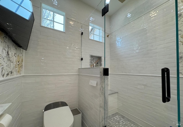 bathroom featuring toilet, a stall shower, tile walls, and wainscoting