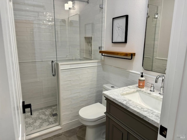 bathroom with tile walls, toilet, a stall shower, vanity, and tile patterned floors