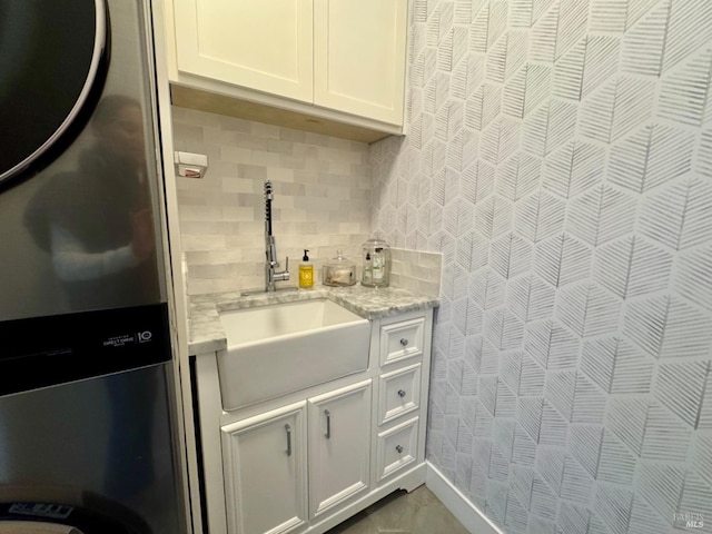 kitchen featuring tasteful backsplash, light stone counters, refrigerator, white cabinetry, and a sink