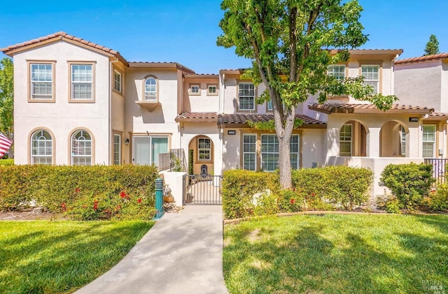 mediterranean / spanish-style home featuring a tiled roof, a gate, a front lawn, and stucco siding