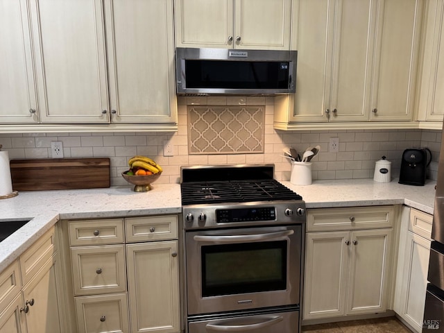 kitchen featuring light stone countertops, tasteful backsplash, appliances with stainless steel finishes, and cream cabinetry