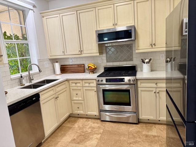 kitchen featuring stainless steel appliances, cream cabinets, backsplash, and a sink