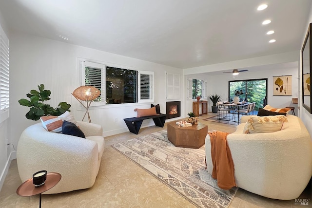 living area with baseboards, a lit fireplace, ceiling fan, and recessed lighting