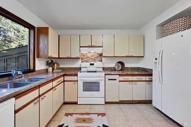 kitchen with cream cabinets, light tile patterned flooring, a sink, white appliances, and under cabinet range hood