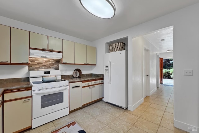 kitchen with cream cabinets, under cabinet range hood, white appliances, decorative backsplash, and dark countertops