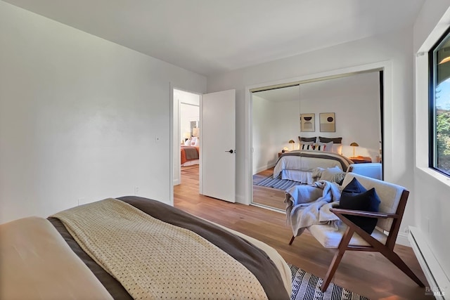 bedroom with a closet, a baseboard radiator, wood finished floors, and baseboards