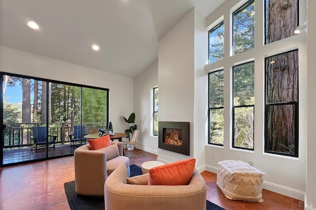 living area featuring high vaulted ceiling, recessed lighting, a glass covered fireplace, and baseboards