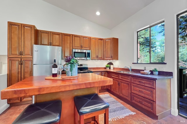 kitchen with a breakfast bar, appliances with stainless steel finishes, brown cabinetry, a sink, and a kitchen island