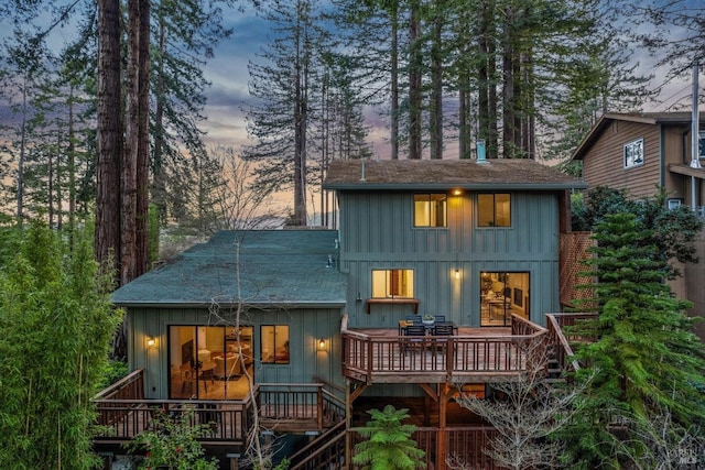 back of house at dusk with a deck and board and batten siding