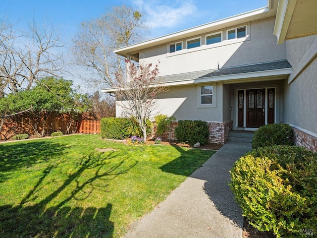 doorway to property with brick siding, a lawn, fence, and stucco siding