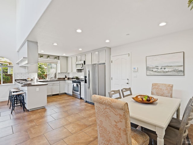 kitchen featuring recessed lighting, a peninsula, appliances with stainless steel finishes, backsplash, and wall chimney exhaust hood