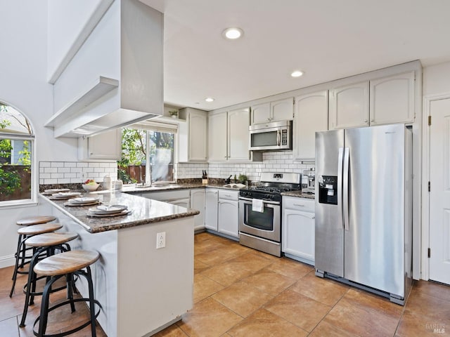 kitchen with a peninsula, plenty of natural light, tasteful backsplash, and appliances with stainless steel finishes