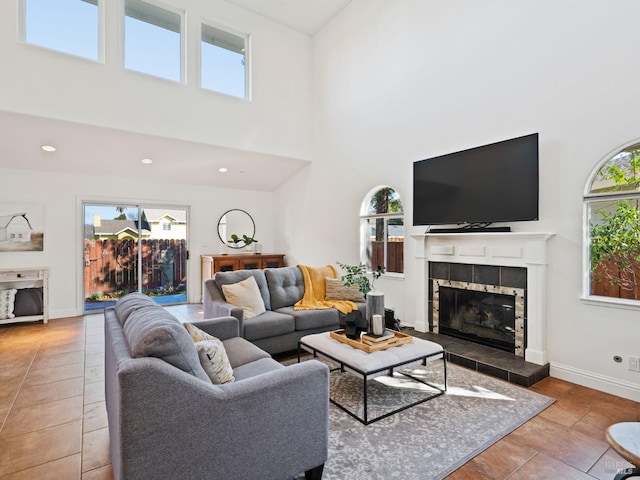 living area with baseboards, a tiled fireplace, a towering ceiling, tile patterned floors, and recessed lighting