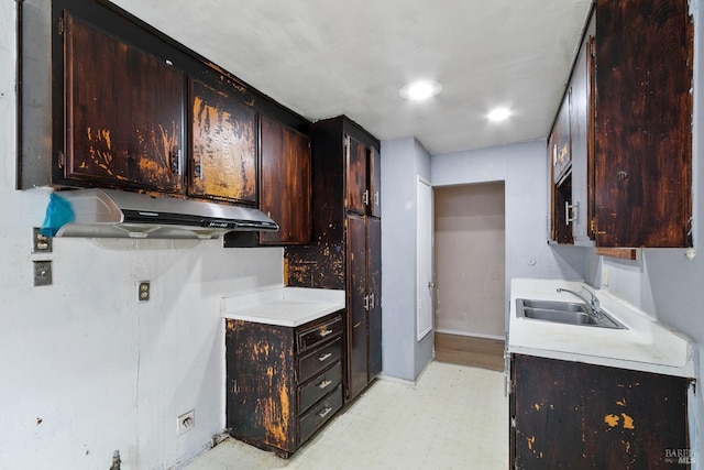 kitchen featuring dark brown cabinetry, light floors, light countertops, under cabinet range hood, and a sink