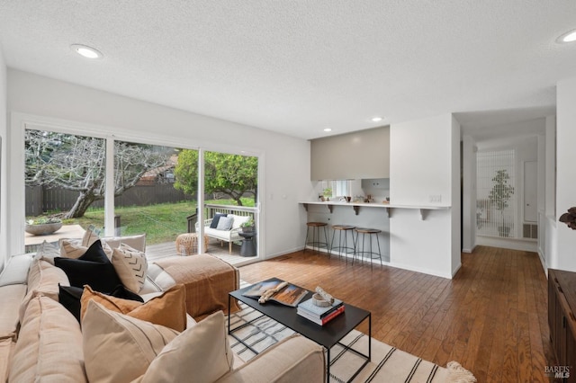 living area featuring visible vents, baseboards, wood-type flooring, a textured ceiling, and recessed lighting