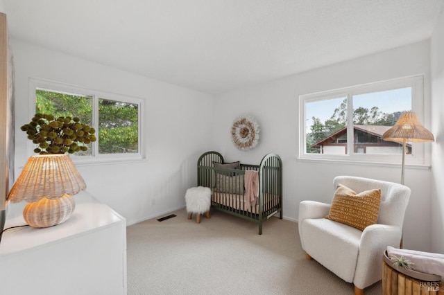 carpeted bedroom with a nursery area, visible vents, and baseboards