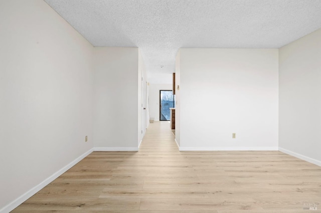 empty room with a textured ceiling, light wood-type flooring, and baseboards