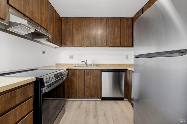 kitchen with light countertops, appliances with stainless steel finishes, a sink, light wood-type flooring, and under cabinet range hood