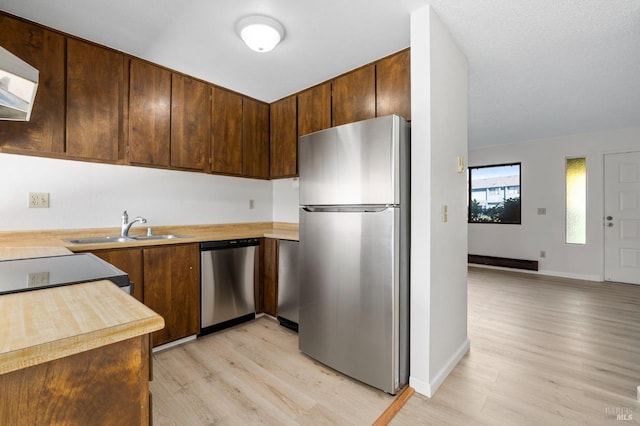 kitchen featuring baseboards, appliances with stainless steel finishes, light wood-type flooring, wall chimney range hood, and a sink