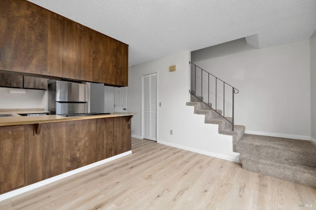 kitchen with light countertops, freestanding refrigerator, a textured ceiling, light wood-type flooring, and baseboards