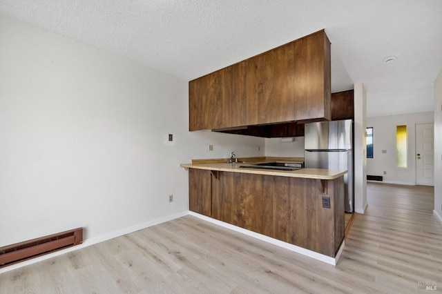 kitchen with brown cabinetry, a baseboard radiator, freestanding refrigerator, light countertops, and a kitchen bar