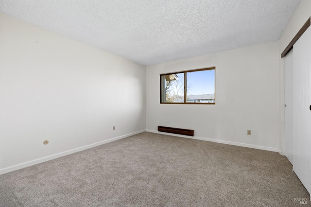 carpeted spare room featuring a textured ceiling and baseboards