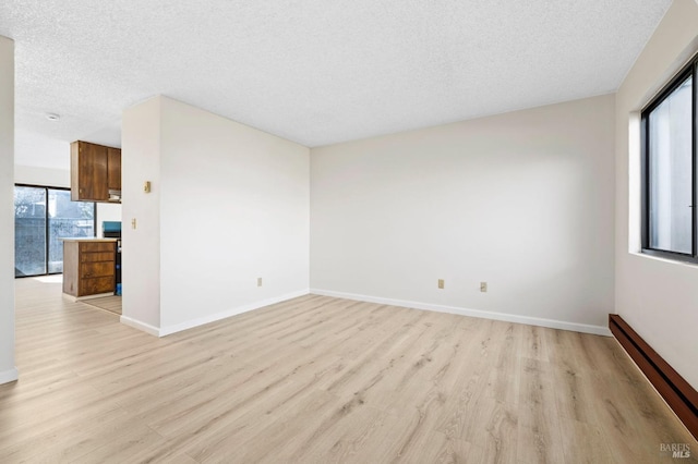 spare room with a textured ceiling, a baseboard radiator, baseboards, and light wood-style floors