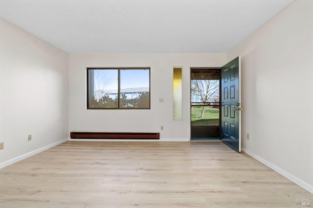 unfurnished room with baseboard heating, light wood-type flooring, and baseboards