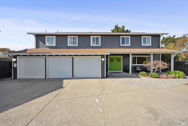 traditional-style house featuring a garage, concrete driveway, roof with shingles, and fence