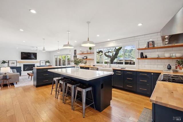 kitchen featuring butcher block countertops, a breakfast bar area, wall chimney range hood, a fireplace, and open shelves