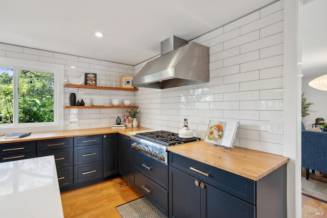 kitchen with stainless steel gas cooktop, wood counters, wall chimney range hood, light wood-type flooring, and backsplash