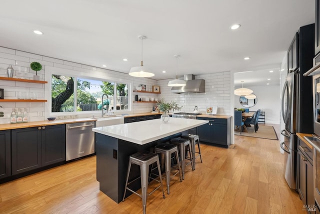 kitchen featuring a breakfast bar area, open shelves, a sink, appliances with stainless steel finishes, and wall chimney exhaust hood