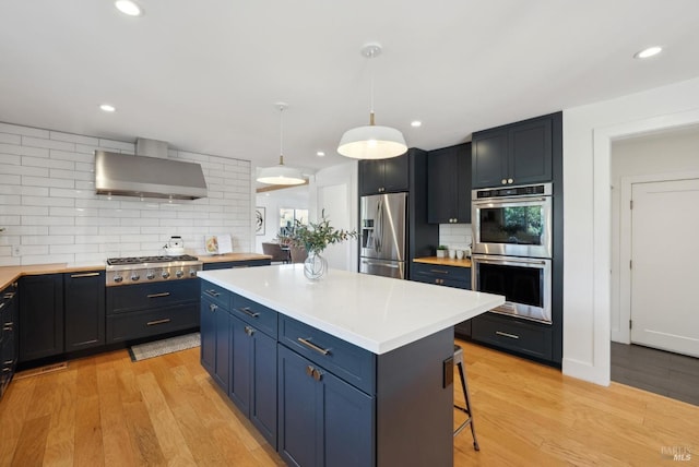 kitchen with light countertops, appliances with stainless steel finishes, light wood-type flooring, and wall chimney range hood