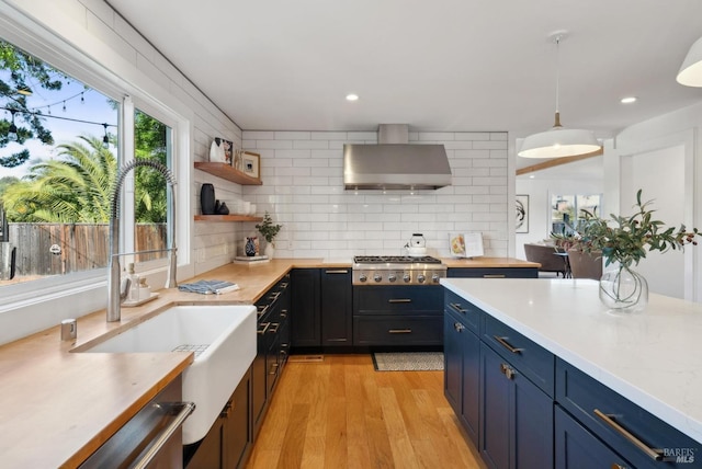 kitchen featuring stainless steel gas cooktop, blue cabinetry, tasteful backsplash, light countertops, and wall chimney exhaust hood