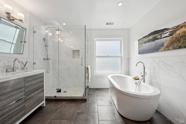 full bathroom featuring a marble finish shower, visible vents, vanity, a freestanding tub, and tile walls