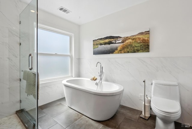 bathroom with tile walls, a marble finish shower, visible vents, a freestanding bath, and toilet