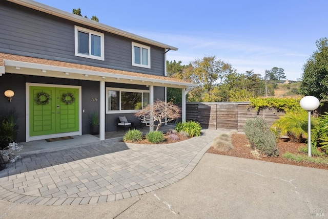 exterior space with a shingled roof, covered porch, fence, and stucco siding