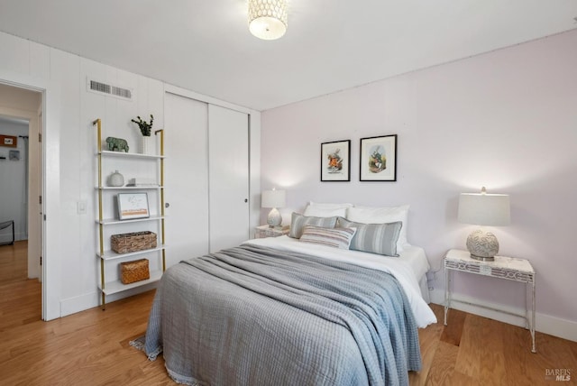 bedroom with a closet, wood finished floors, visible vents, and baseboards